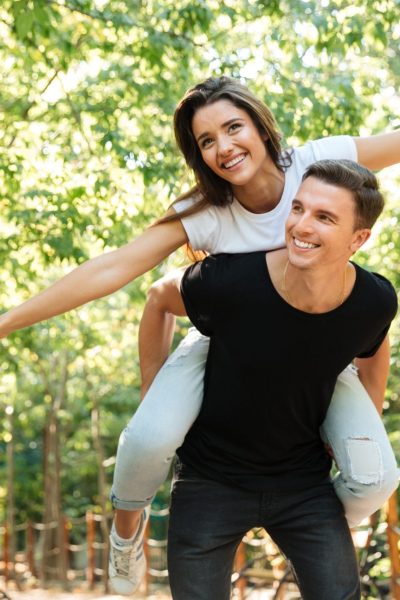 Young smiling couple enjoying piggyback ride and laughing at the park outdoors